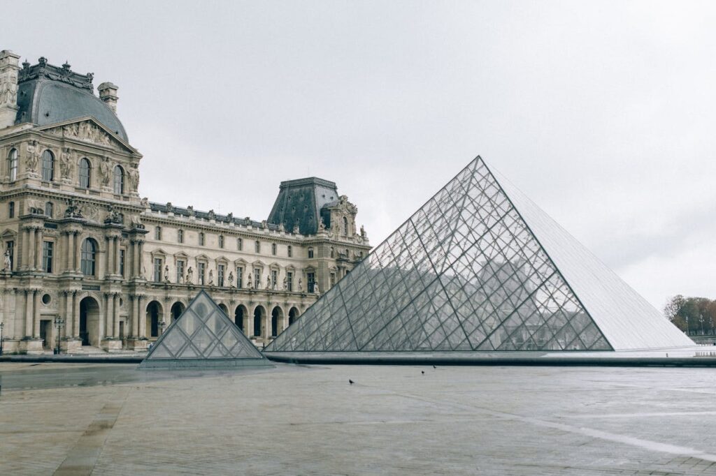 The iconic Louvre Museum with its glass pyramid on a cloudy day in Paris, France.